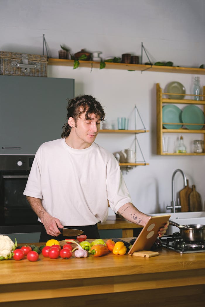 Man using a tablet to follow a recipe while preparing fresh vegetables in a contemporary kitchen.