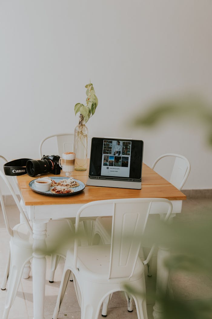 Inviting workspace setup indoors featuring coffee, laptop, camera, and meal on a wooden table.
