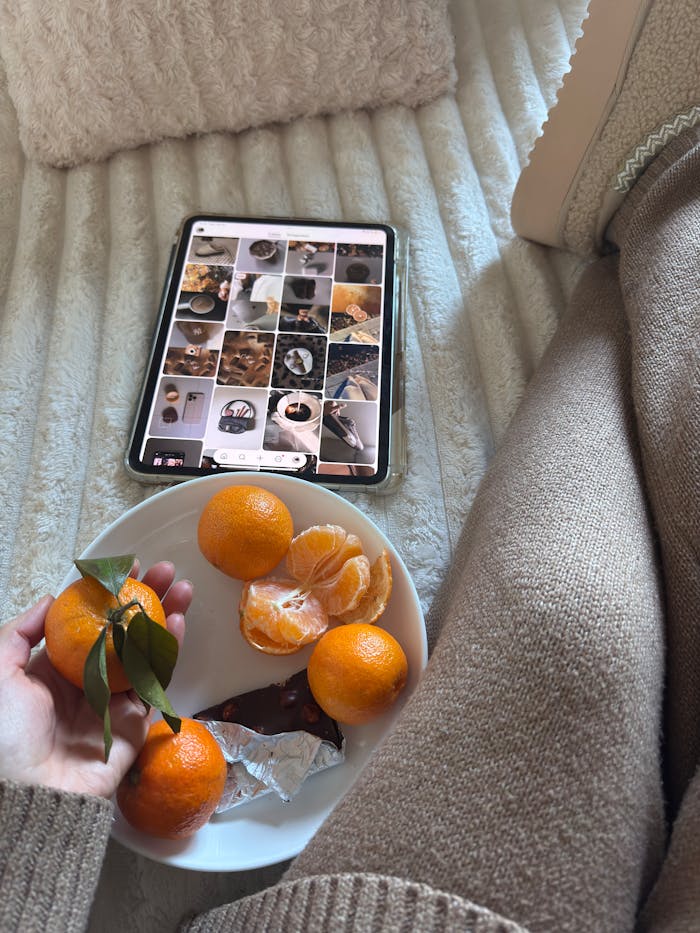 A warm, cozy setup with a tablet, oranges, and chocolate on a bed, ideal for relaxation.